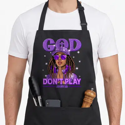 African christian apron - Cartoon woman praying below purple GOD text with cross in O and DON'T PLAY ABOUT ME caption — shown on a black cotton canvas apron against a white background