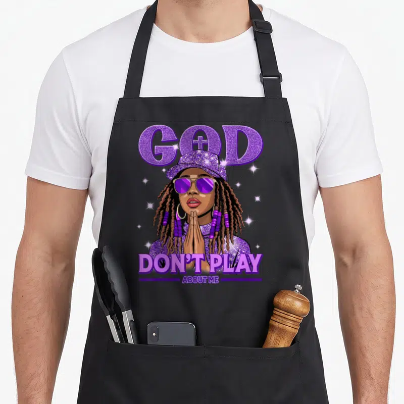 African christian apron - Cartoon woman praying below purple GOD text with cross in O and DON'T PLAY ABOUT ME caption — shown on a black cotton canvas apron against a white background