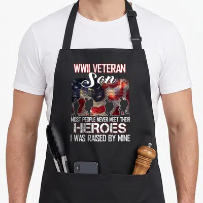 Son people meet apron - WWII VETERAN Son text above four soldier silhouettes against a red white blue flag and fireworks — shown on a black cotton canvas apron against a white background