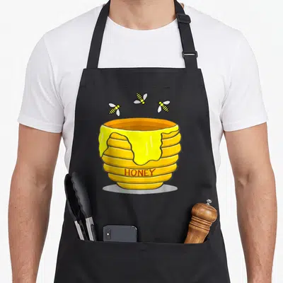 Pot honey bee apron - Cartoon honey pot with HONEY text and three flying bees — shown on a black cotton canvas apron against a white background