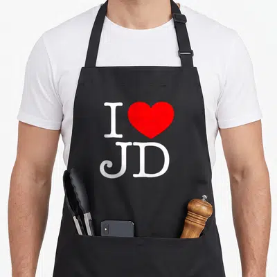 Funny jd apron - White I and red heart above JD letters — shown on a black cotton canvas apron against a white background