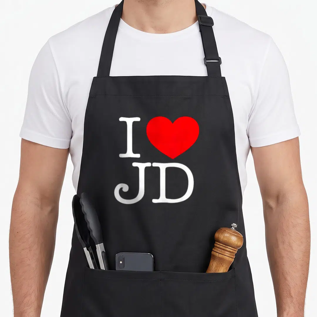 Funny jd apron - White I and red heart above JD letters — shown on a black cotton canvas apron against a white background