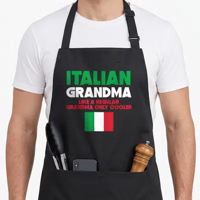 Grandma italian apron - Four lines of green, white, and red text above a centered Italian flag — shown on a black cotton canvas apron against a white background
