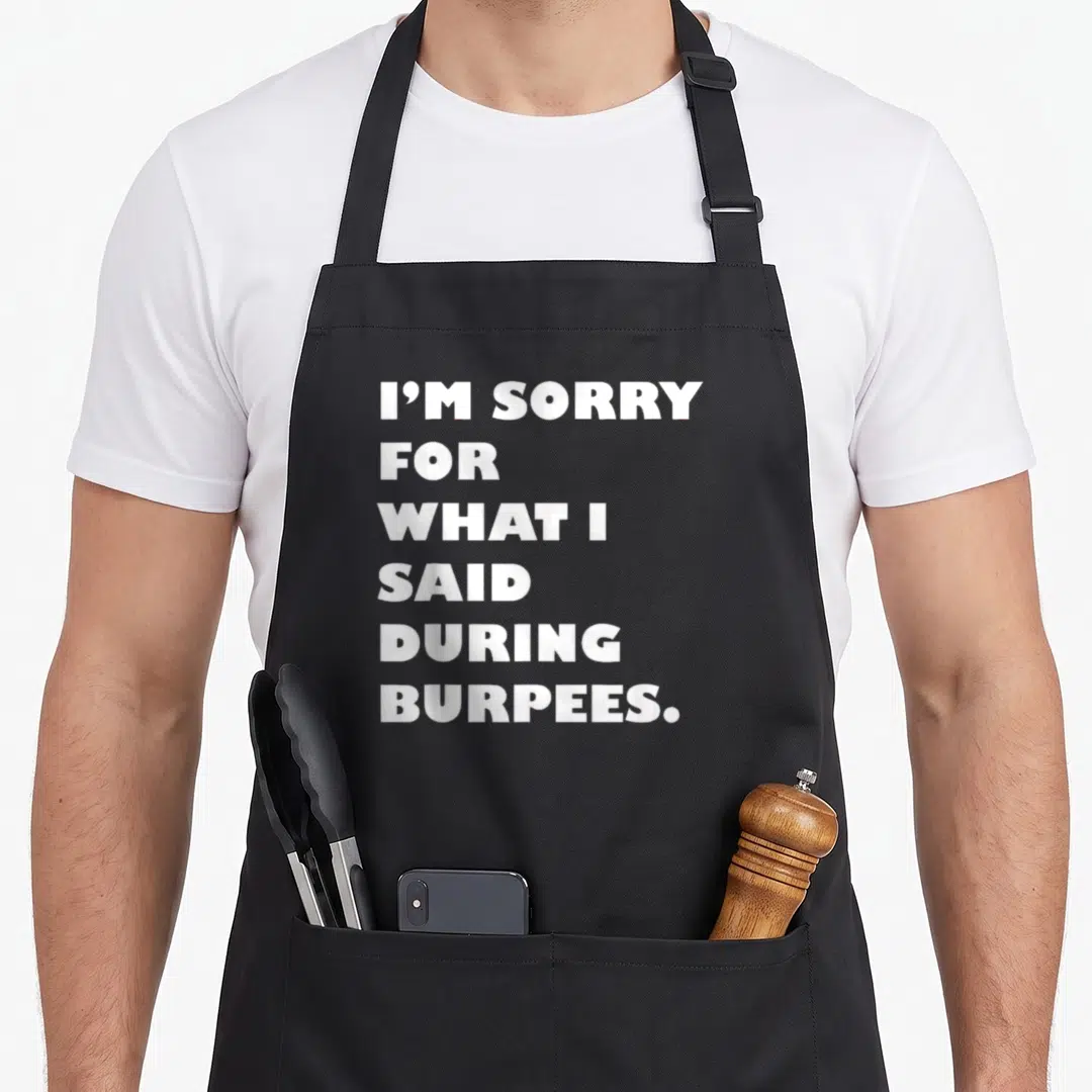 Funny sorry burpees apron - White text reading I'm sorry for what I said during burpees stacked in six lines — shown on a black cotton canvas apron against a white background