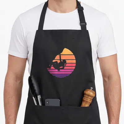 Climb climbing apron - Aerial silks silhouette against a striped sunset in yellow orange pink purple — shown on a black cotton canvas apron against a white background