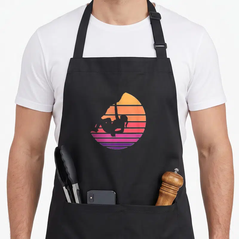 Climb climbing apron - Aerial silks silhouette against a striped sunset in yellow orange pink purple — shown on a black cotton canvas apron against a white background