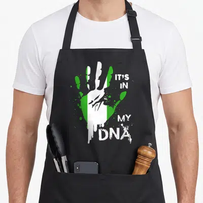 Dna nigerian apron - Handprint with green white stripes and IT'S IN MY DNA text — shown on a black cotton canvas apron against a white background