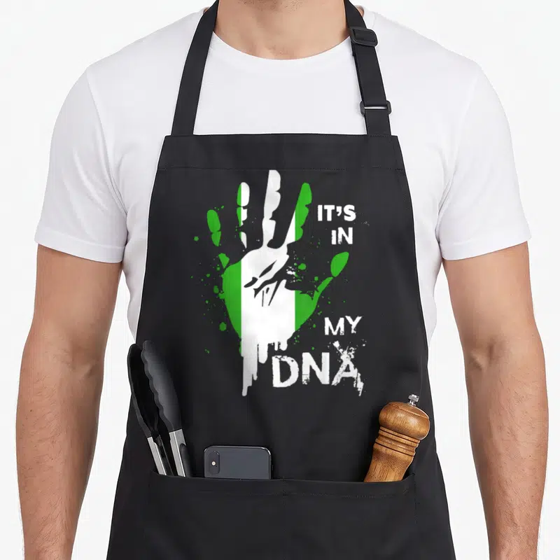 Dna nigerian apron - Handprint with green white stripes and IT'S IN MY DNA text — shown on a black cotton canvas apron against a white background
