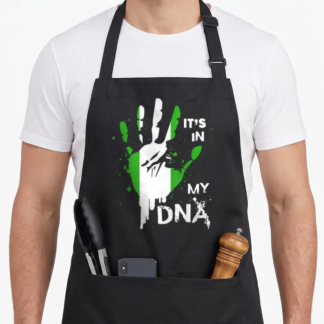 Dna nigerian apron - Handprint with green white stripes and IT'S IN MY DNA text — shown on a black cotton canvas apron against a white background