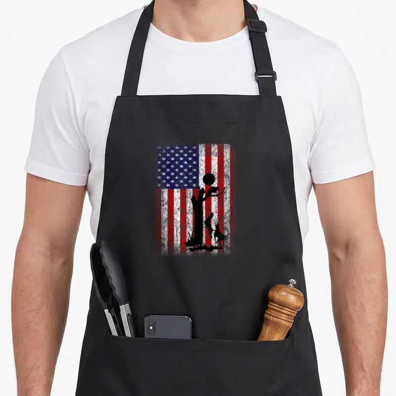Coon patriotic aprons - Distressed USA flag with black silhouette of tree, moon, cat in branches, and two dogs at base — shown on a black cotton canvas apron against a white background