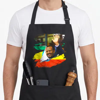 Abiy dr apron - Photo of man waving over green yellow red blue white flag brush strokes — shown on a black cotton canvas apron against a white background