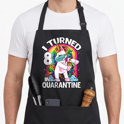 Turned unicorn apron - I TURNED 8 IN QUARANTINE text with masked flossing unicorn and rainbow — shown on a black cotton canvas apron against a white background