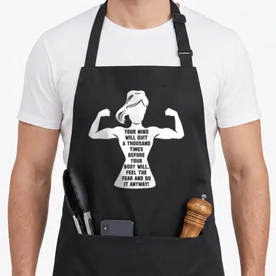 Gym bodybuilding apron - White silhouette of a flexing woman with text about mind quitting before body — shown on a black cotton canvas apron against a white background