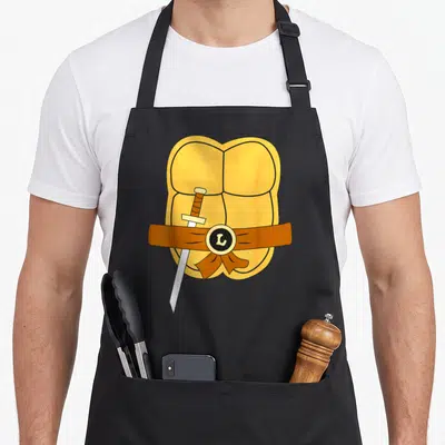 Leonardo easy apron - Yellow cartoon torso with brown belt silver sword and L buckle — shown on a black cotton canvas apron against a white background