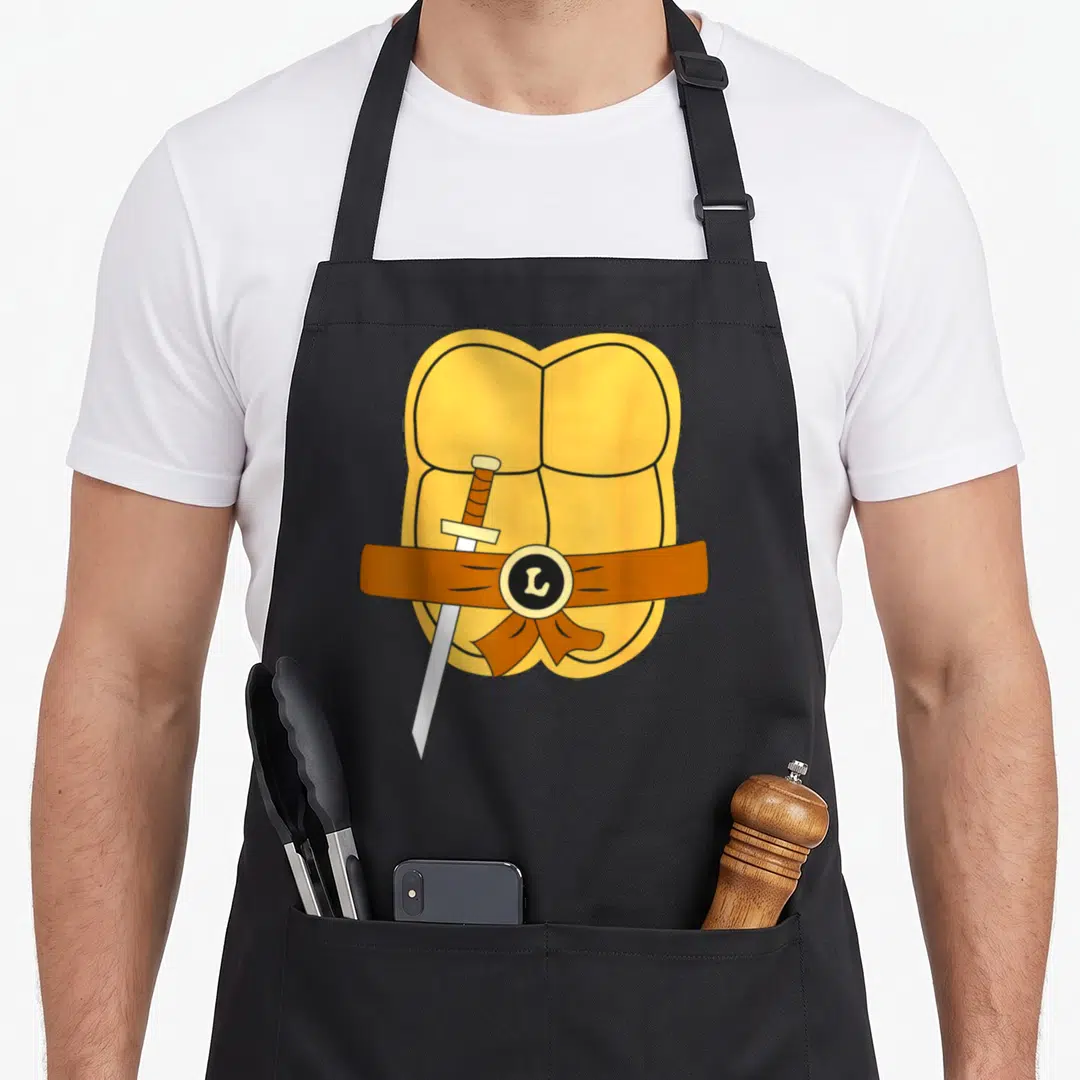 Leonardo easy apron - Yellow cartoon torso with brown belt silver sword and L buckle — shown on a black cotton canvas apron against a white background
