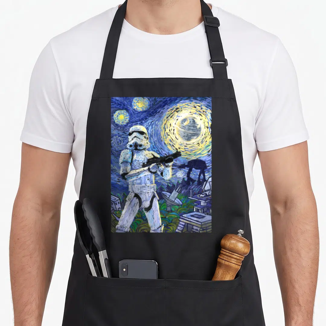 Starry nights apron - Watercolor Stormtrooper blaster Death Star AT-AT swirling blue sky yellow stars — shown on a black cotton canvas apron against a white background