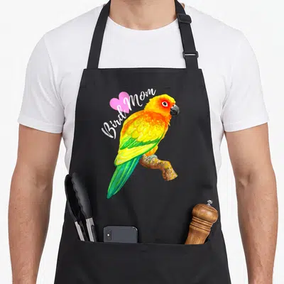 Parrot sun bird apron - Watercolor sun conure parrot perched on branch with Bird Mom text and pink heart — shown on a black cotton canvas apron against a white background