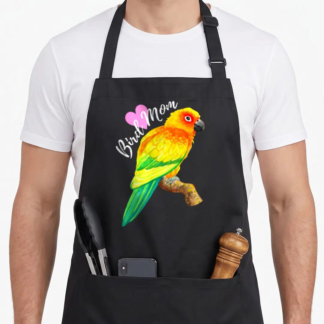 Parrot sun bird apron - Watercolor sun conure parrot perched on branch with Bird Mom text and pink heart — shown on a black cotton canvas apron against a white background