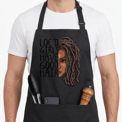 Loc hair apron - Loc'd Girls Have Good Hair text beside cartoon woman face with brown dreadlocks — shown on a black cotton canvas apron against a white background