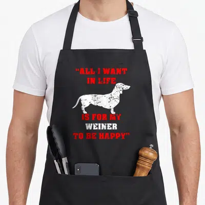 Dachshund dog trainer apron - Red and white text about a wiener surrounding a white dachshund silhouette — shown on a black cotton canvas apron against a white background