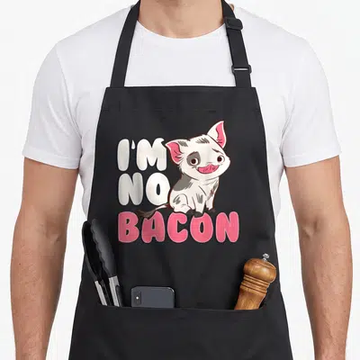 Pua bacon apron - Cartoon pig sitting next to I'm No Bacon text in white and pink — shown on a black cotton canvas apron against a white background