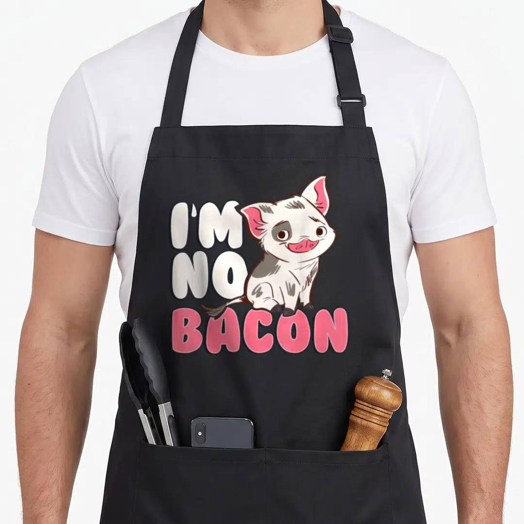Pua bacon apron - Cartoon pig sitting next to I'm No Bacon text in white and pink — shown on a black cotton canvas apron against a white background