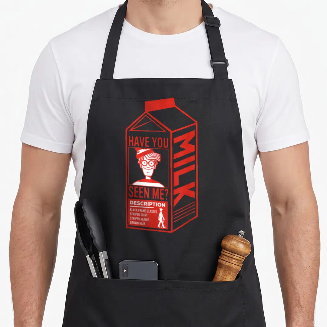 Waldo milk aprons - Red and white milk carton with missing person ad listing striped shirt and glasses — shown on a black cotton canvas apron against a white background