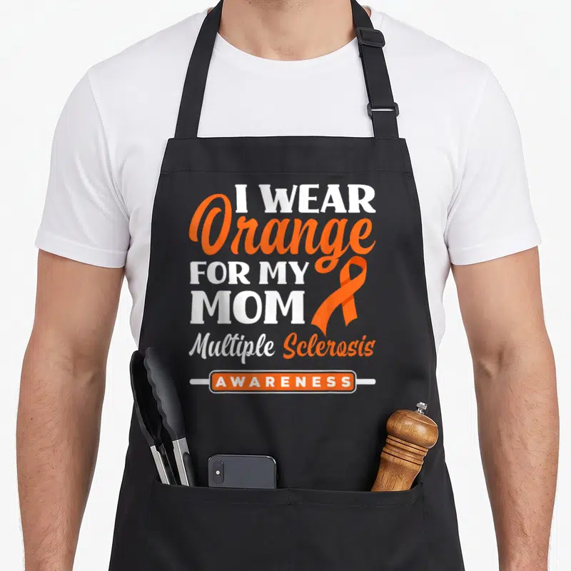 Vintage multiple sclerosis awareness apron - Orange and white text reading I Wear Orange For My Mom Multiple Sclerosis — shown on a black cotton canvas apron against a white background