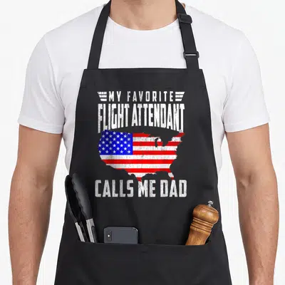 Flight papa apron - Distressed white text My Favorite Flight Attendant Calls Me Dad surrounding a USA map filled — shown on a black cotton canvas apron against a white background