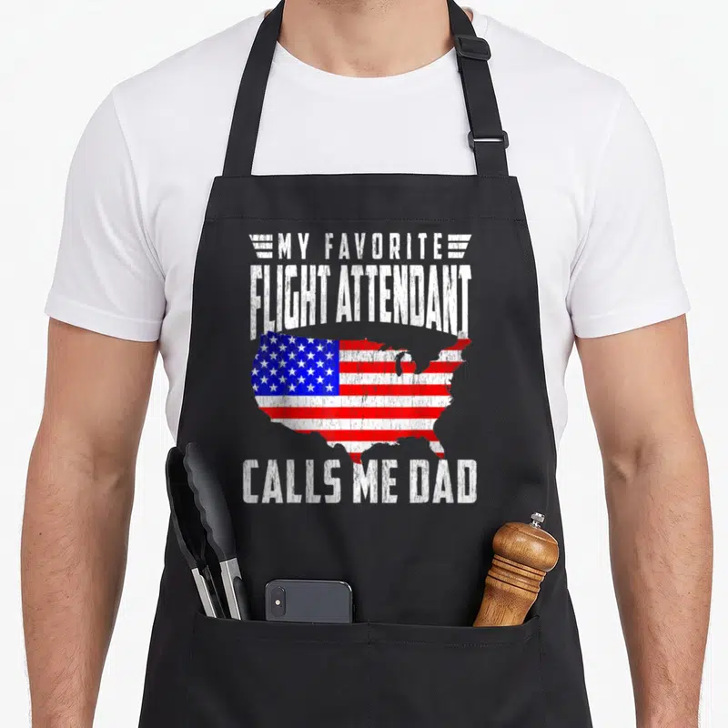Flight papa apron - Distressed white text My Favorite Flight Attendant Calls Me Dad surrounding a USA map filled — shown on a black cotton canvas apron against a white background