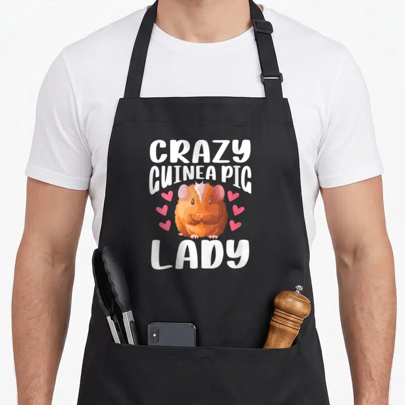 Critter crazy guinea lady apron - Cartoon orange guinea pig with six pink hearts and white text CRAZY GUINEA PIG LADY — shown on a black cotton canvas apron against a white background