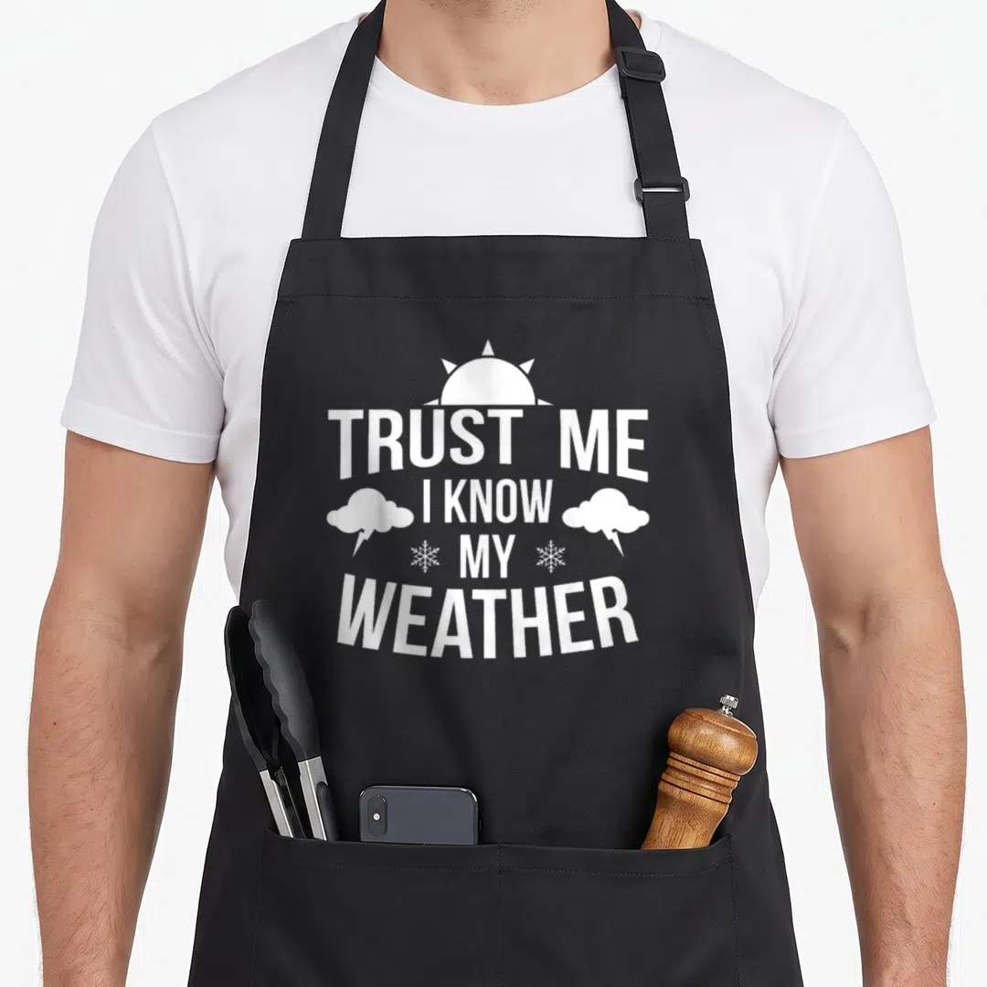 Forecaster meteorologist apron - White stacked text TRUST ME I KNOW MY WEATHER with sun, cloud, and snowflake icons — shown on a black cotton canvas apron against a white background