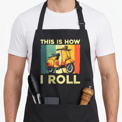 Motor scooter apron - Retro scooter graphic with vertical colored stripes and textTHIS IS HOW I ROLL — shown on a black cotton canvas apron against a white background