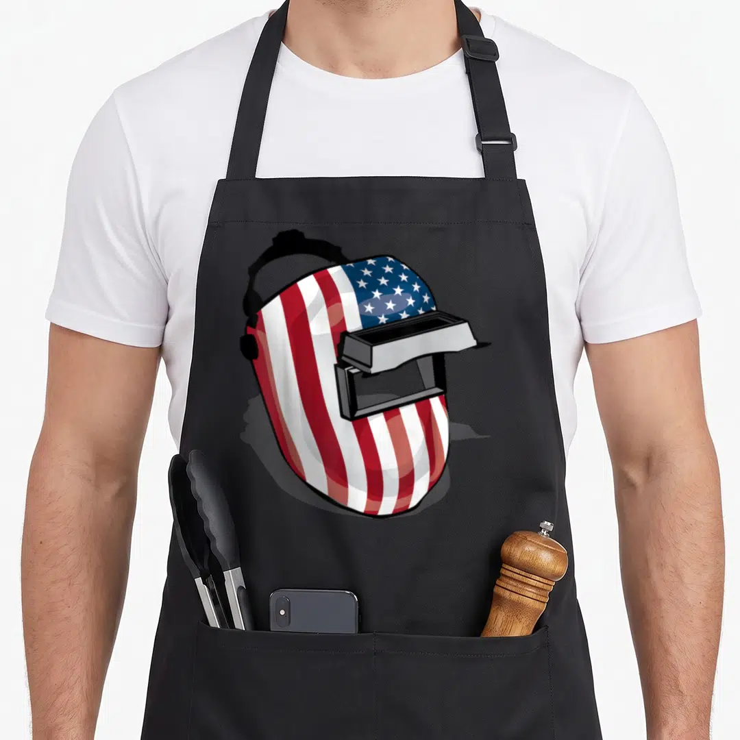 Helmet american flag apron - Welding helmet shaped like US flag in red white blue and black — shown on a black cotton canvas apron against a white background