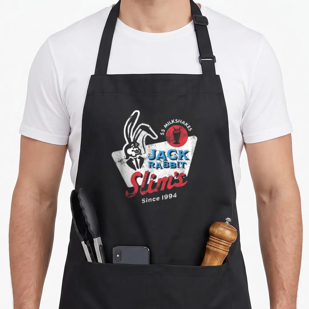 Jack rabbit apron - Retro diner logo with rabbit head, red circle, blue JACK RABBIT text, red Slim's script, and Since — shown on a black cotton canvas apron against a white background