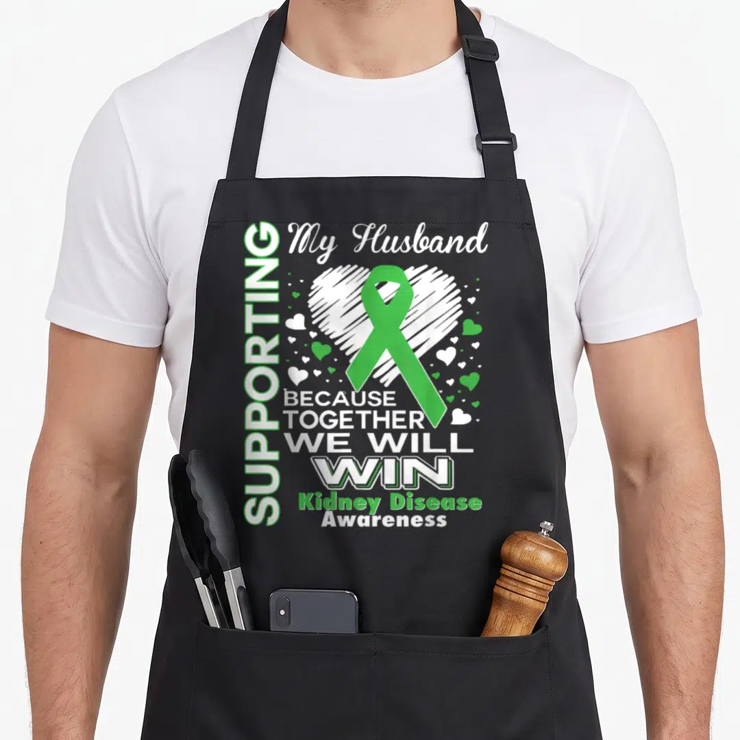 Supporting husband apron - Green ribbon over white sketched heart with supportive typography for kidney disease — shown on a black cotton canvas apron against a white background