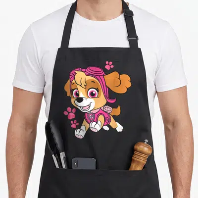 Skye patrol happy apron - Cartoon Skye jumping with three pink glittery paw prints — shown on a black cotton canvas apron against a white background