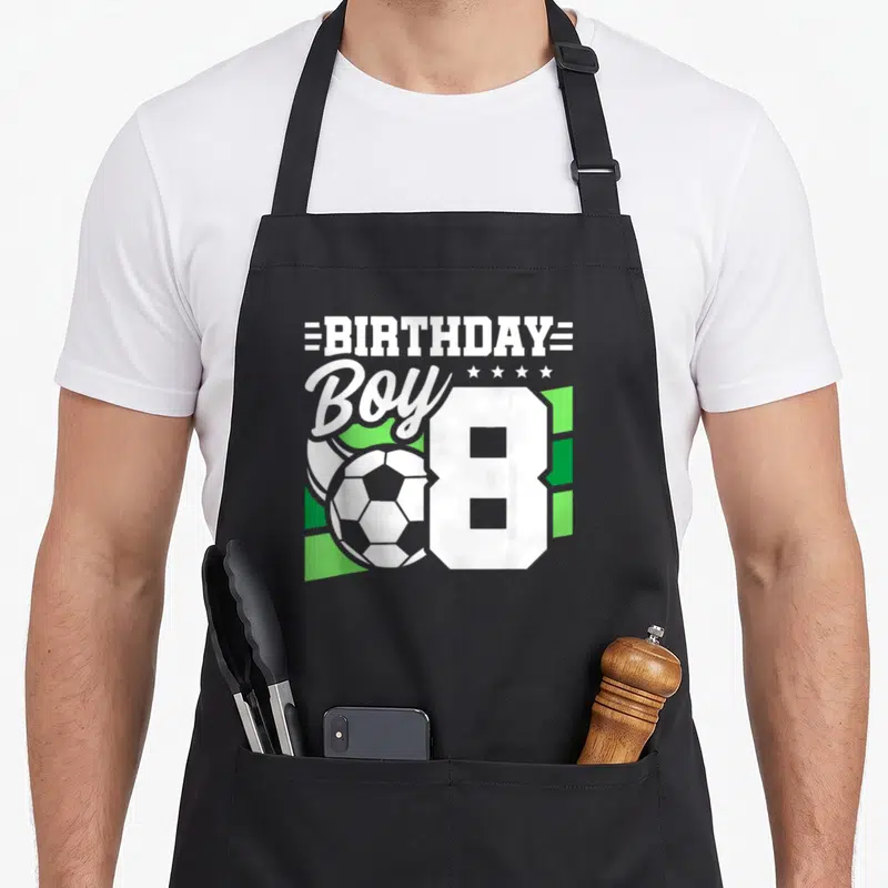 Soccer 8th birthday apron - White typography BIRTHDAY BOY 8 with soccer ball and green geometric shapes — shown on a black cotton canvas apron against a white background