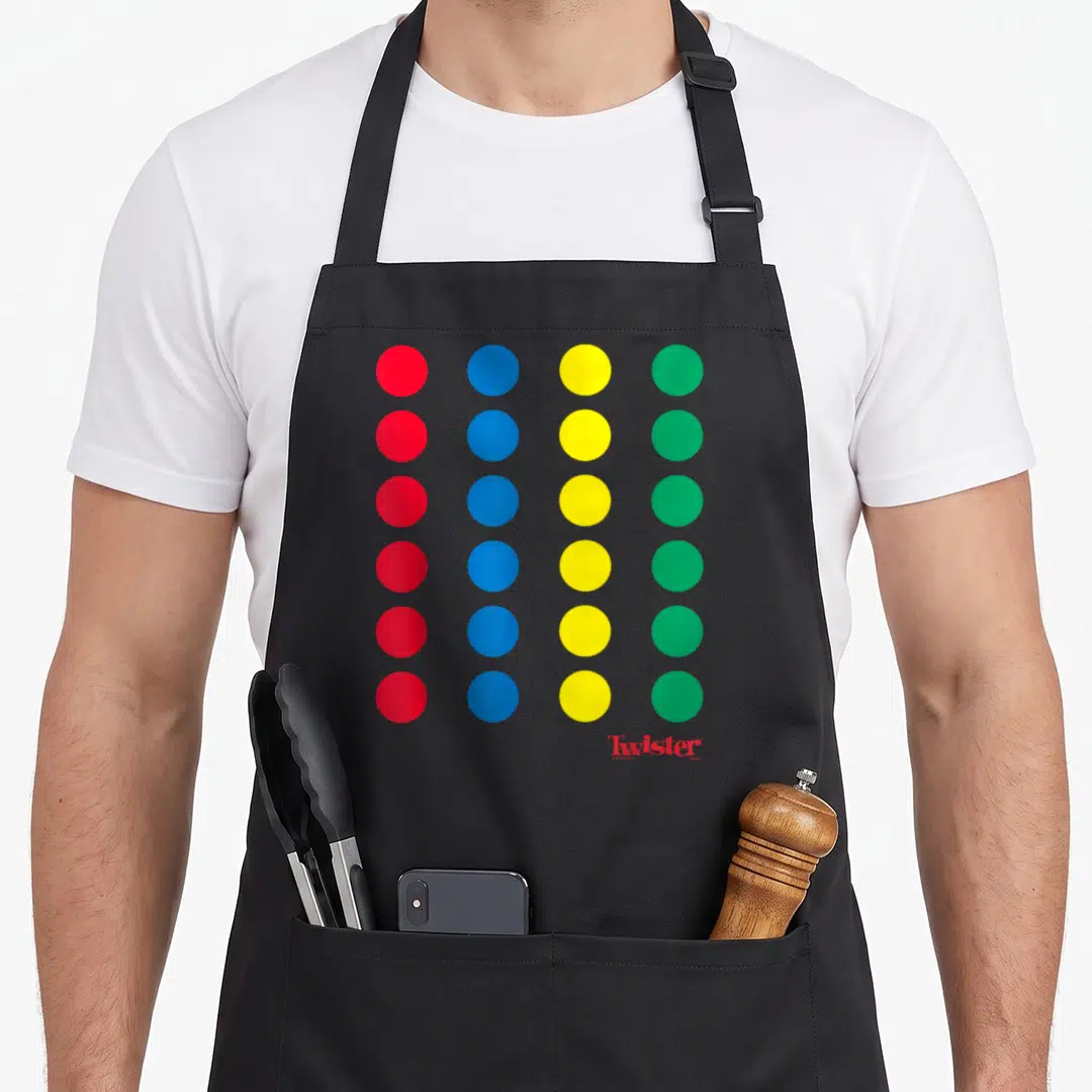 Twister halloween apron - Grid of red blue yellow green dots with Twister logo and copyright text below — shown on a black cotton canvas apron against a white background