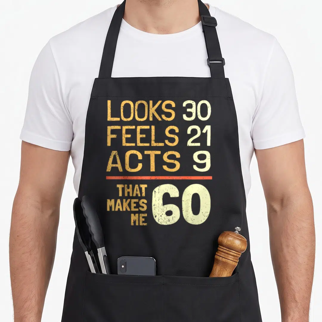 Hilarious 60th birthday apron - Orange and cream typography reading looks 30 feels 21 acts 9 that makes me 60 — shown on a black cotton canvas apron against a white background
