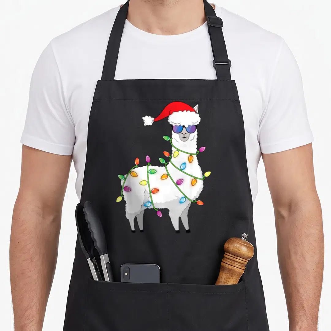 Llama christmas tree apron - White llama in red Santa hat and blue sunglasses wrapped in colorful Christmas lights — shown on a black cotton canvas apron against a white background