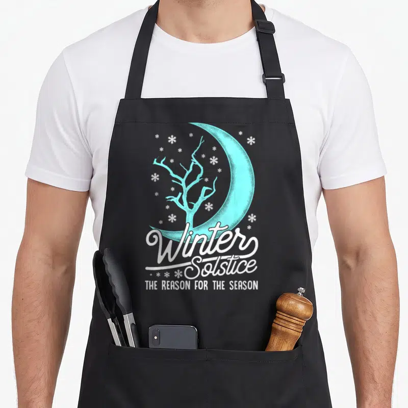 Event winter apron - Light blue crescent moon and leafless tree with white snowflakes and Winter Solstice text — shown on a black cotton canvas apron against a white background