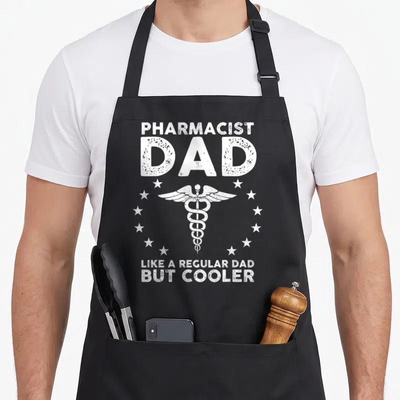 School pharmacy pharmacist apron - White distressed PHARMACIST DAD text and caduceus surrounded by stars — shown on a black cotton canvas apron against a white background
