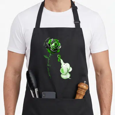 Elephant kidney disease awareness apron - Cartoon elephant holding green ribbon below a rose with vertical script text — shown on a black cotton canvas apron against a white background