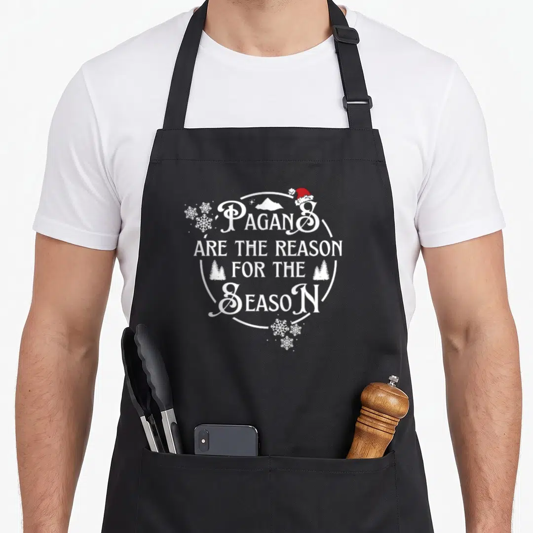 Reason retro christmas aprons - PAGANS ARE THE REASON FOR THE SEASON text with red hat and white snowflakes — shown on a black cotton canvas apron against a white background