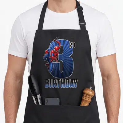 Comic birthday apron - Spider-Man over blue number 3 with RD BIRTHDAY text in cartoon style — shown on a black cotton canvas apron against a white background