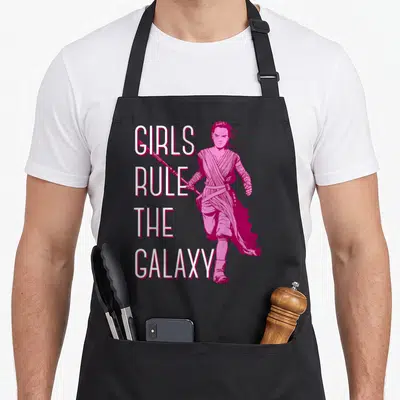 Episode nebula apron - Magenta cartoon woman holding a staff next to stacked white text reading Girls Rule The Galaxy — shown on a black cotton canvas apron against a white background