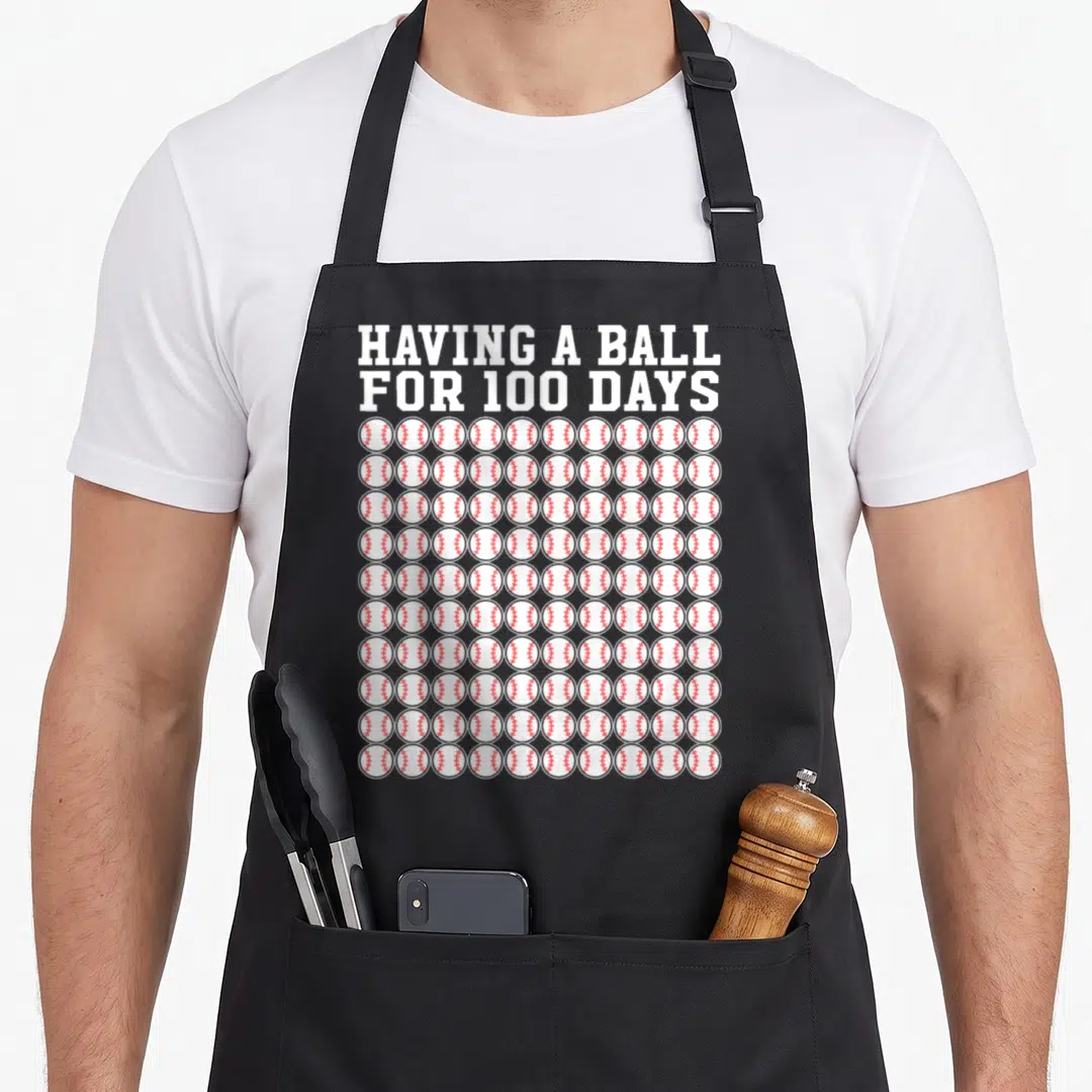 Player teacher apron - Having A Ball For 100 Days text above 100 baseballs with red stitching — shown on a black cotton canvas apron against a white background