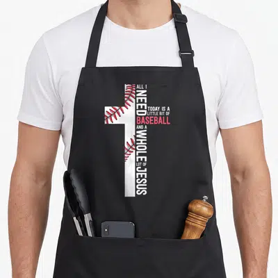 Baseball jesus christian apron - White cross with red stitching and vertical text reading ALL I NEED TODAY IS A LITTLE — shown on a black cotton canvas apron against a white background