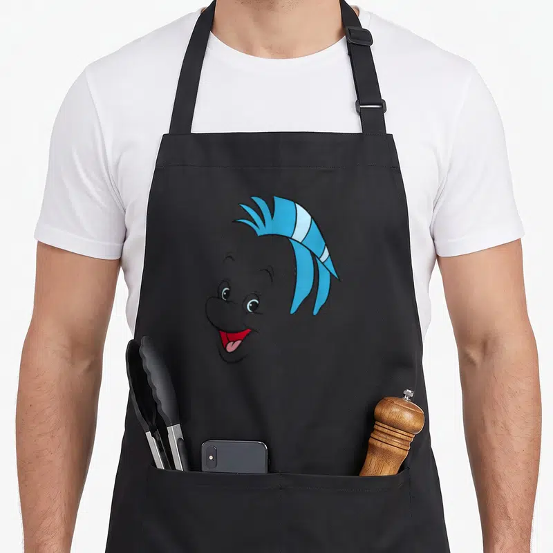 Flounder face apron - Grey cartoon character head with blue crest hair and red open mouth — shown on a black cotton canvas apron against a white background
